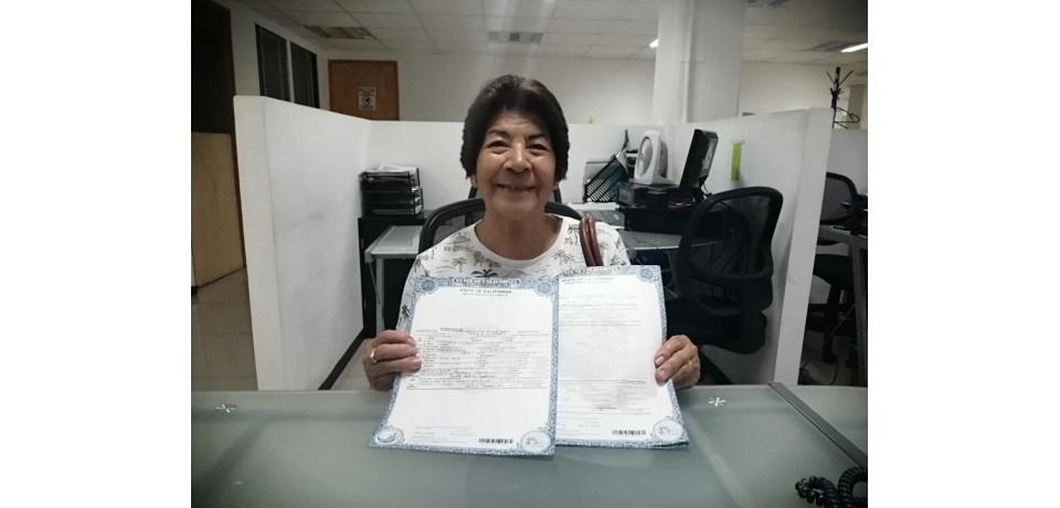 An image of a woman smiling and holding up two approved assistance forms