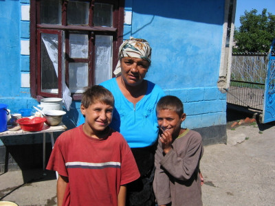 Woman and two young boys stand outside of house